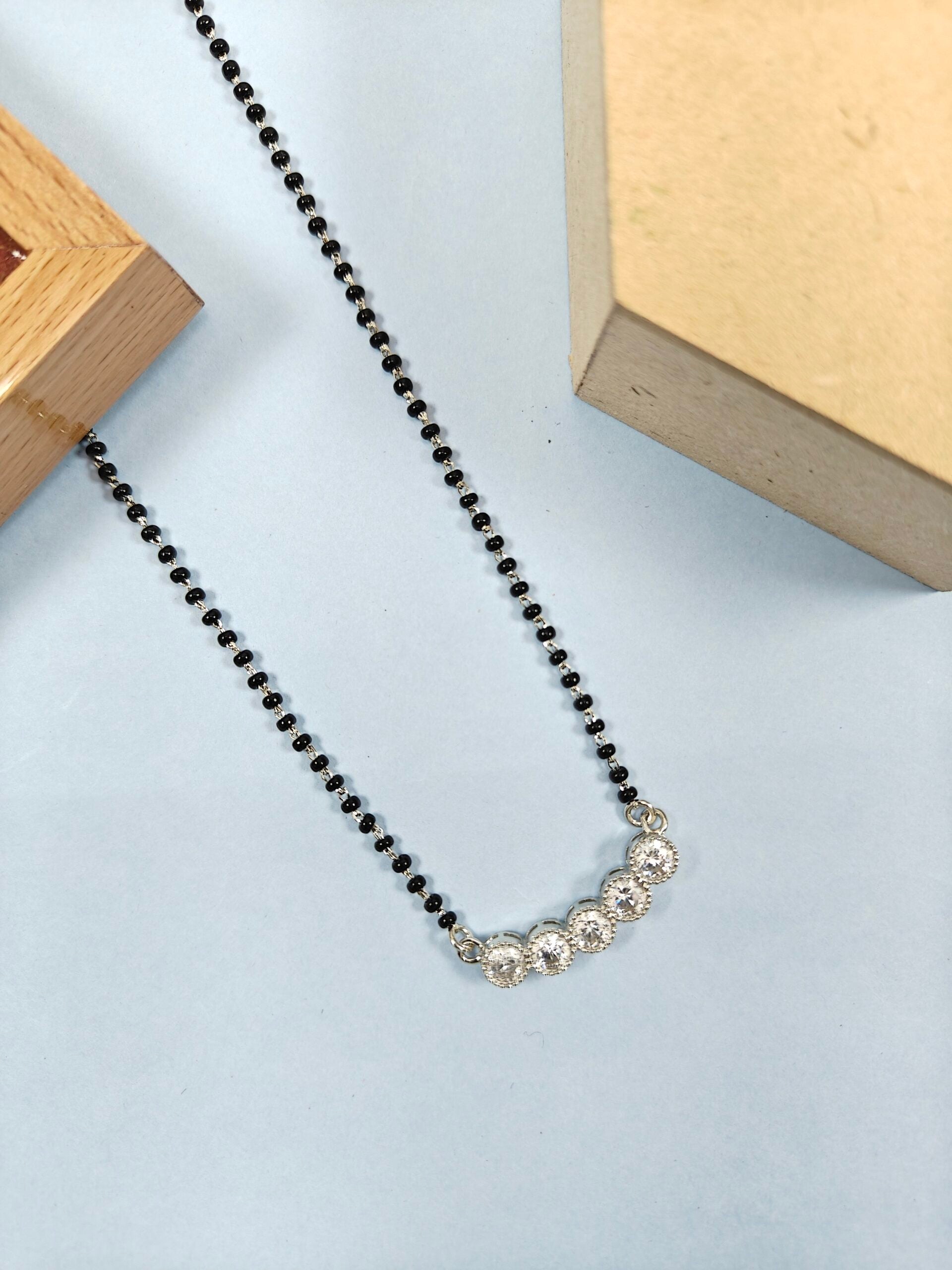 Necklace with black beads and silver pendants on a light blue background